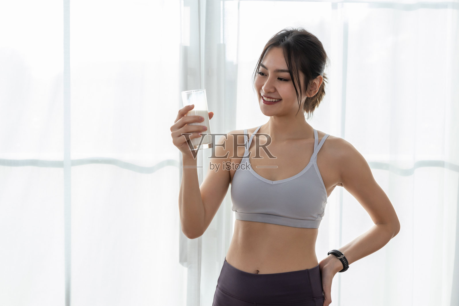 亚洲美丽迷人的女性穿着运动服，手持一杯牛奶，营养健康，适合积极锻炼。含有良好的脂肪，为身体提供能量。牛奶富含钙。照片摄影图片