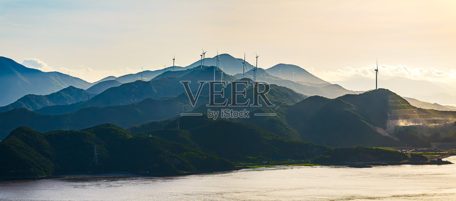 海边的绿色山脊上，风力涡轮机在日出时产生可再生能源。照片摄影图片