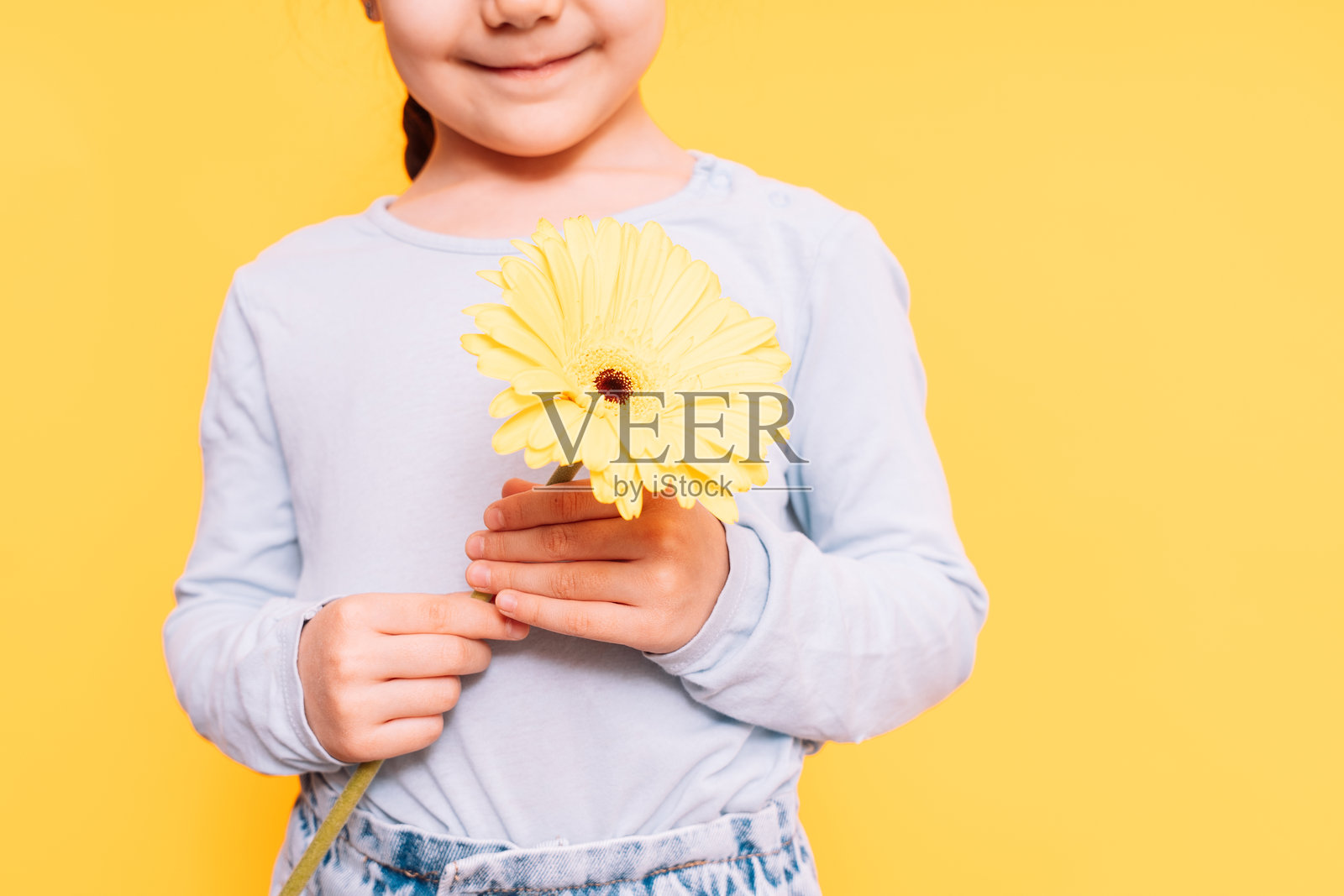 孩子在母亲节假期里双手捧着花，背景是黄色的。照片摄影图片