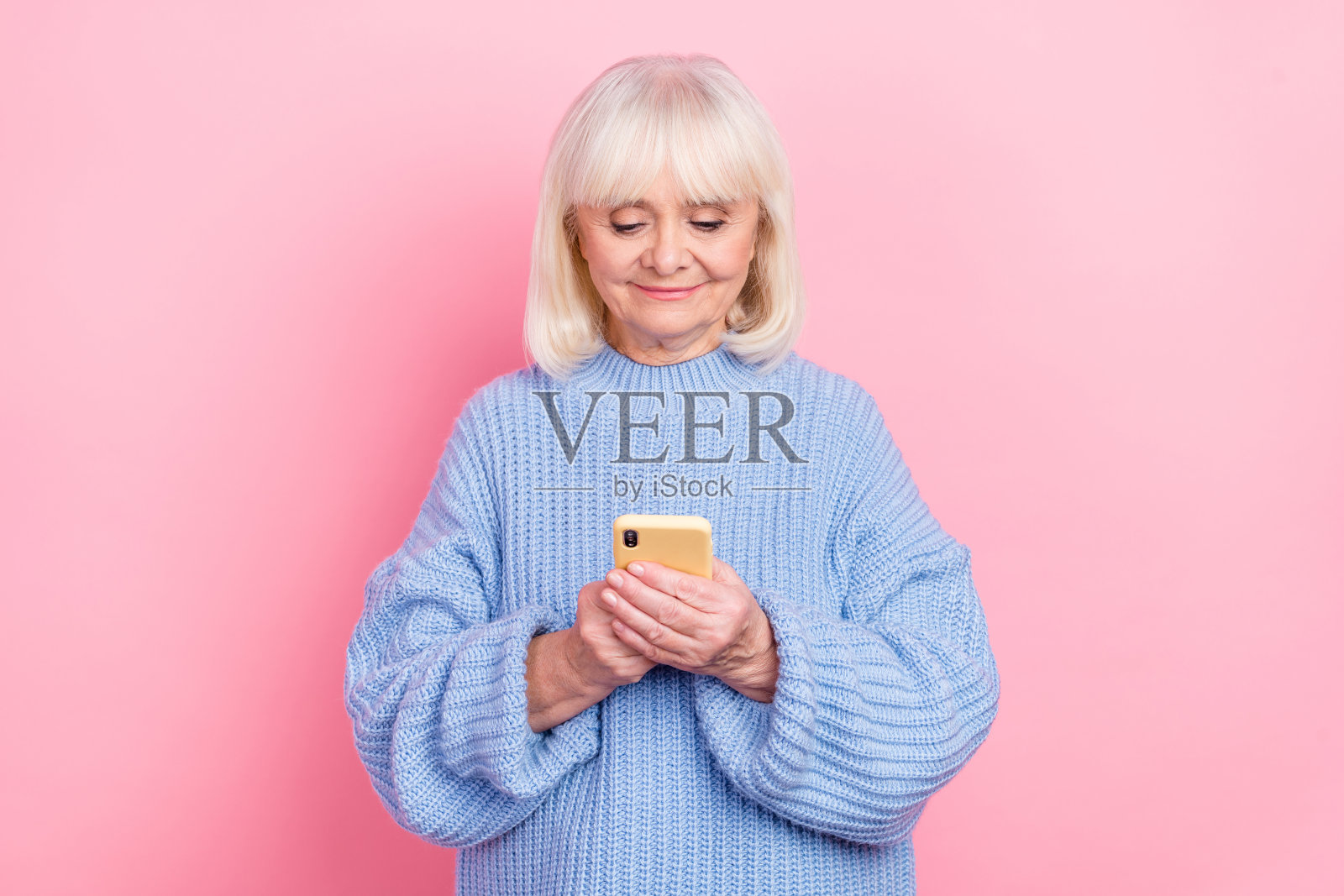 吸引人的专注灰发女性使用设备聊天，社交媒体帖子，背景为粉色柔和色调。照片摄影图片