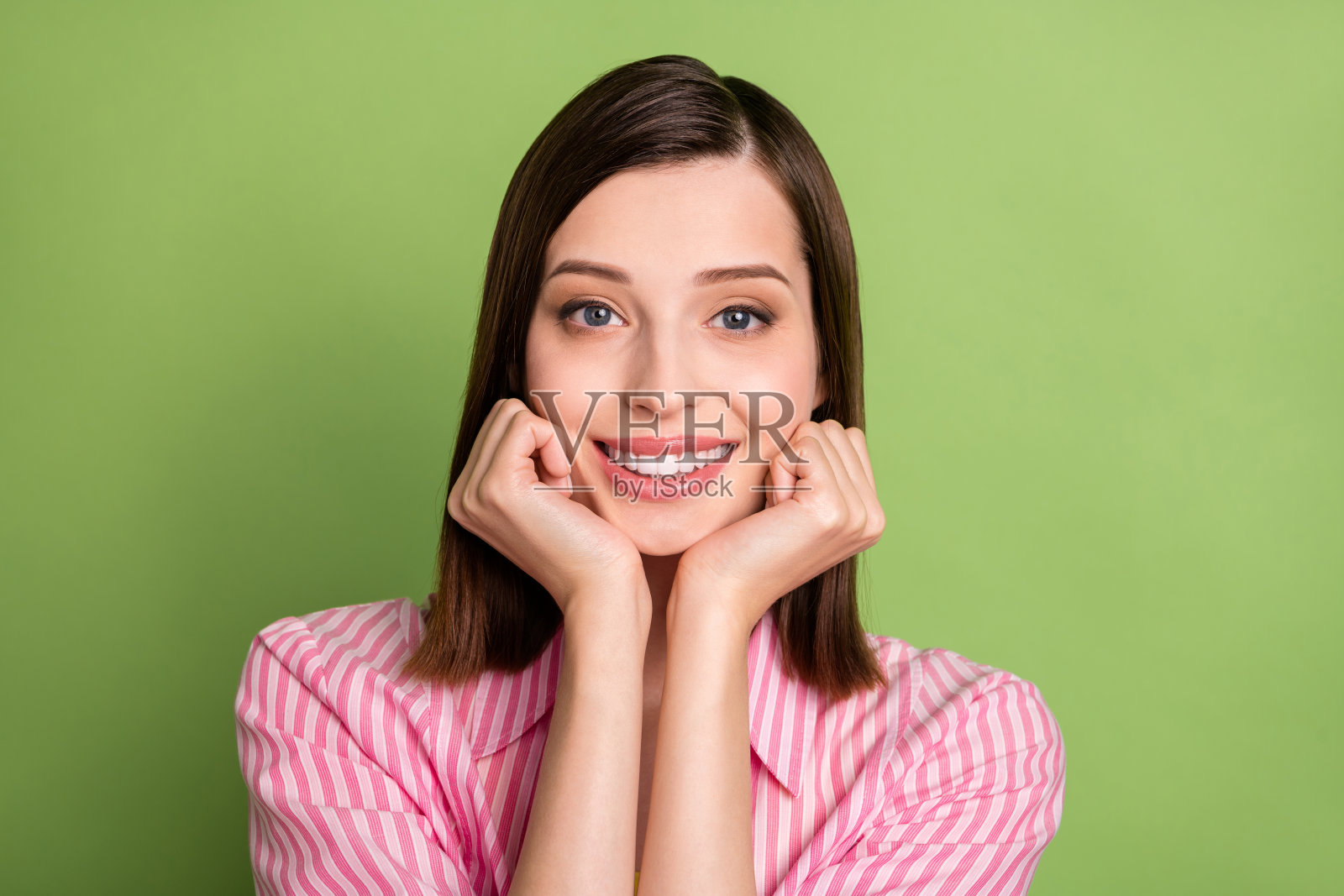 年轻迷人的完美女性双手托着下巴，放松享受闲暇时光，背景为绿色。照片摄影图片