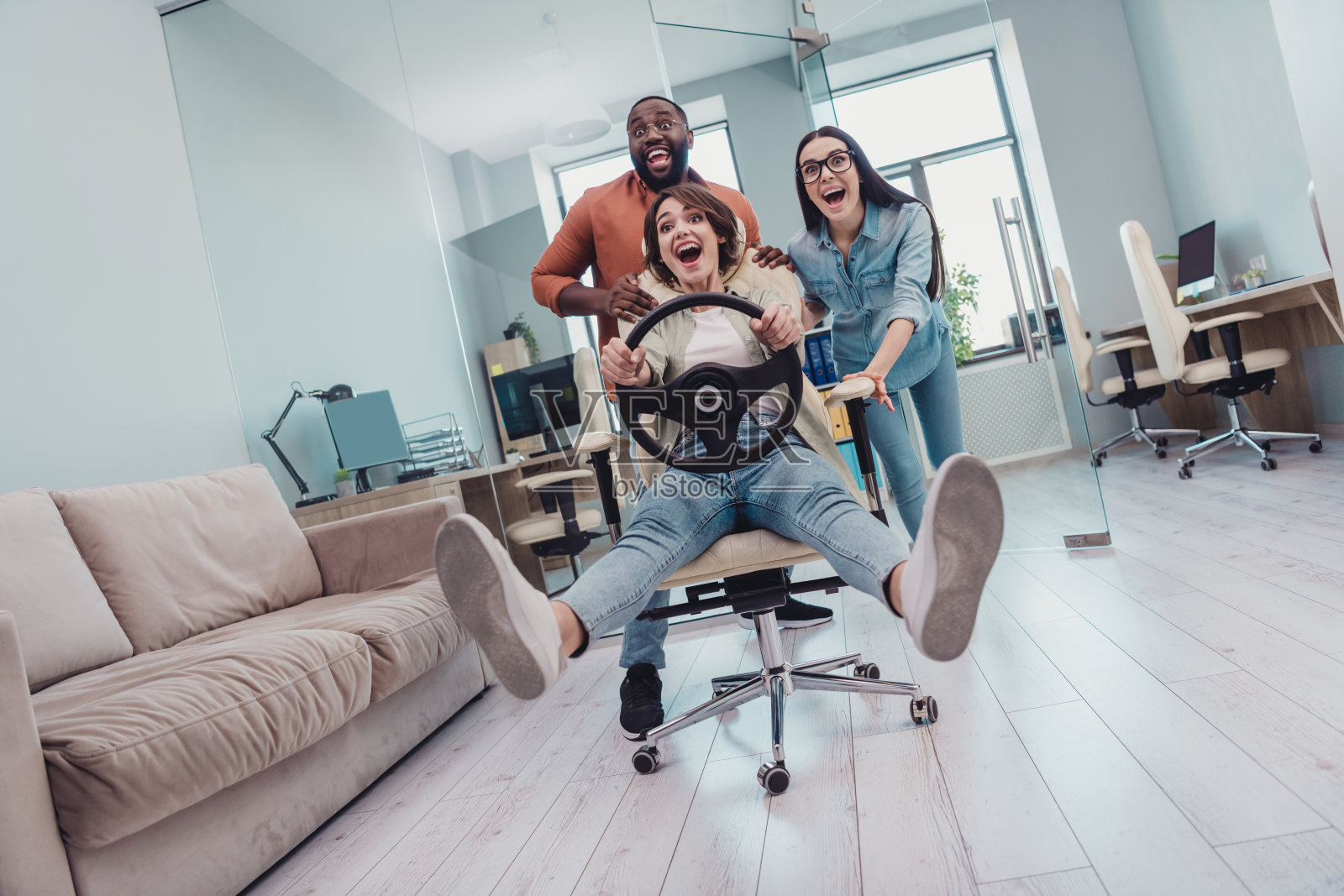 一群迷人的快乐学生在办公室工作站内玩耍，坐在扶手椅上模拟驾驶。照片摄影图片