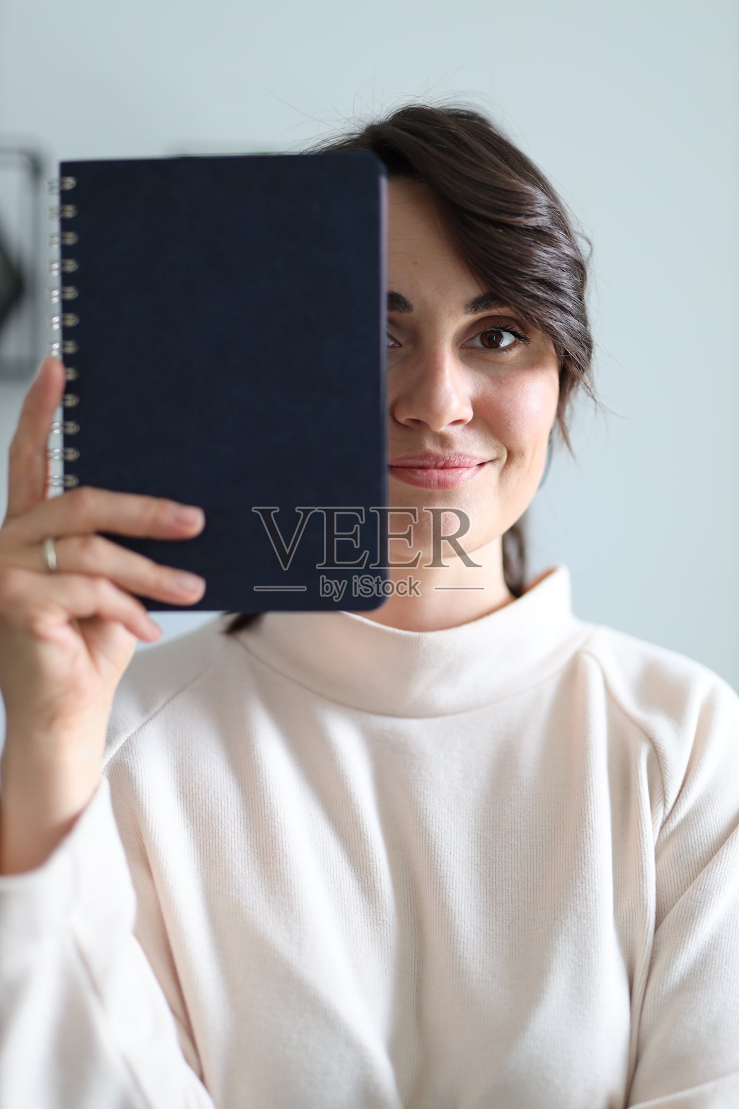 一位女性手持一本蓝色笔记本，面带微笑。笔记本翻开，显示出一个有螺旋装订的页面。照片摄影图片