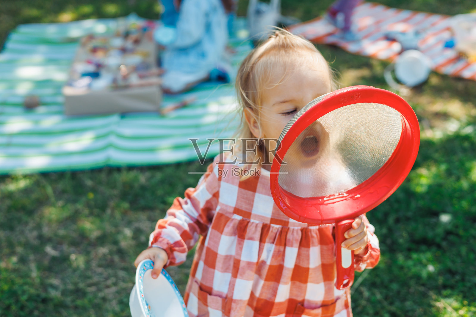 孩子在阳光明媚的公园野餐时玩红色滤网。照片摄影图片