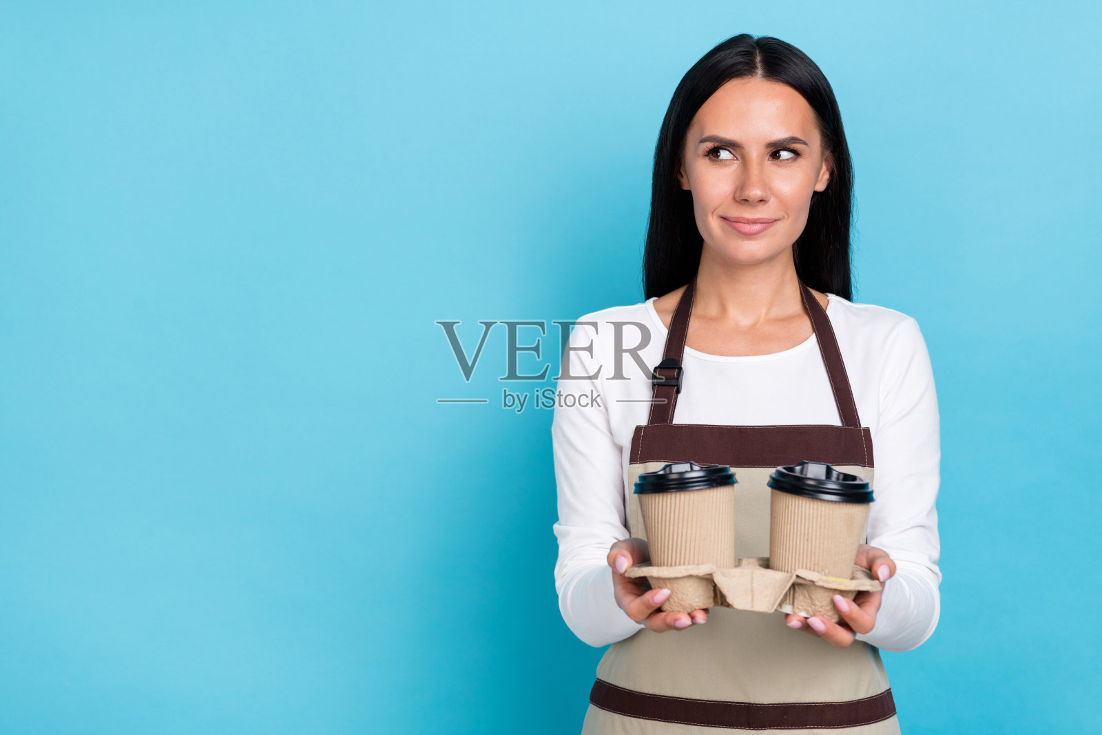 年轻快乐的女性惊讶地看着空旷的空间，手中拿着卡布奇诺咖啡，背景为蓝色。照片摄影图片