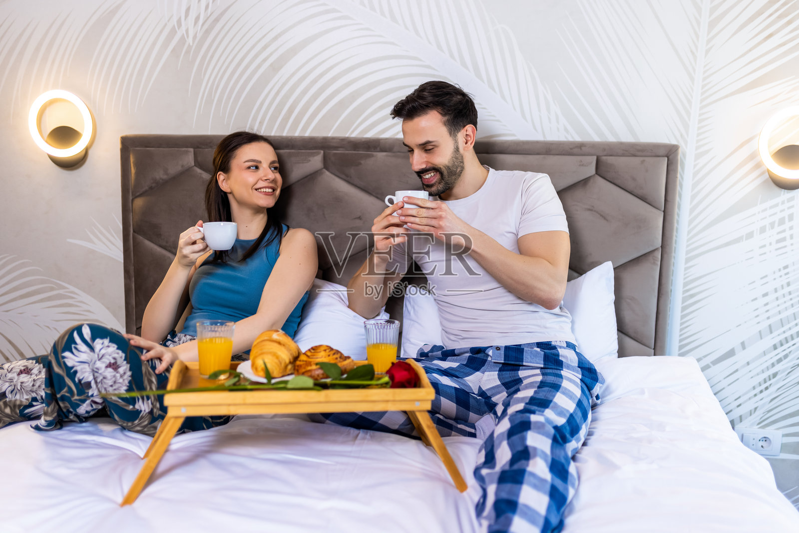 甜蜜的情侣在床上享用早餐。他们喝着咖啡，享受着早晨的时光。照片摄影图片