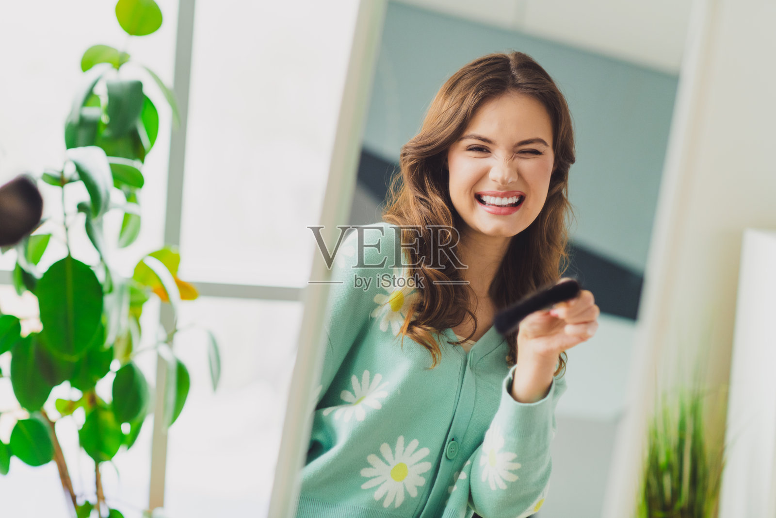 年轻女性面带愉快的微笑，在阳光明媚的室内享受轻松时光，周围环绕着自然光和绿色植物。照片摄影图片