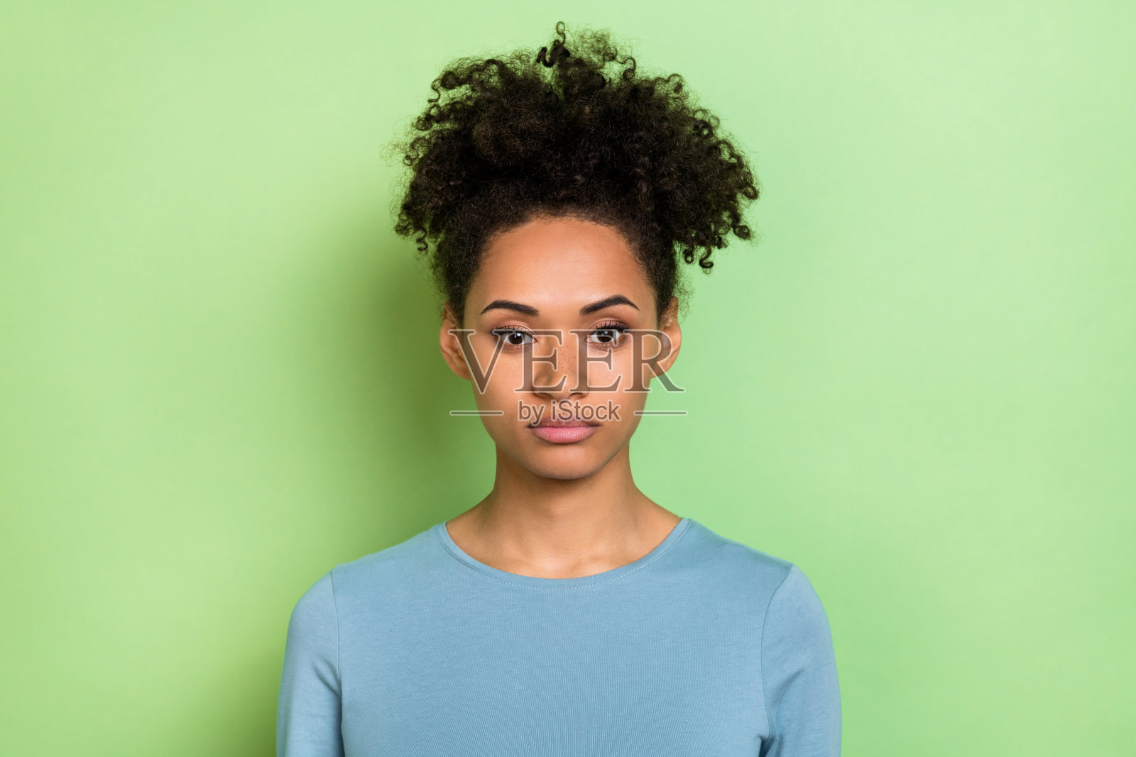 穿着蓝色衬衫的年轻卷发女士，神情严肃自信，背景为绿色。照片摄影图片