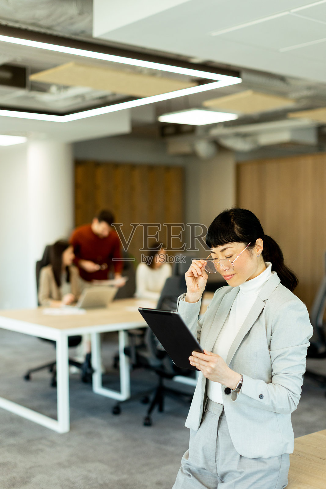 亚洲女商人在现代办公室环境中参加团队会议，专注于平板电脑。照片摄影图片