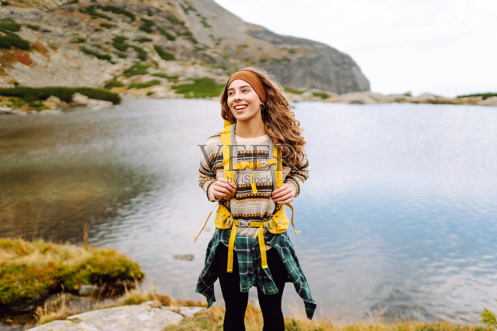 微笑的女性徒步旅行者背着黄色背包，享受山湖风景。照片摄影图片