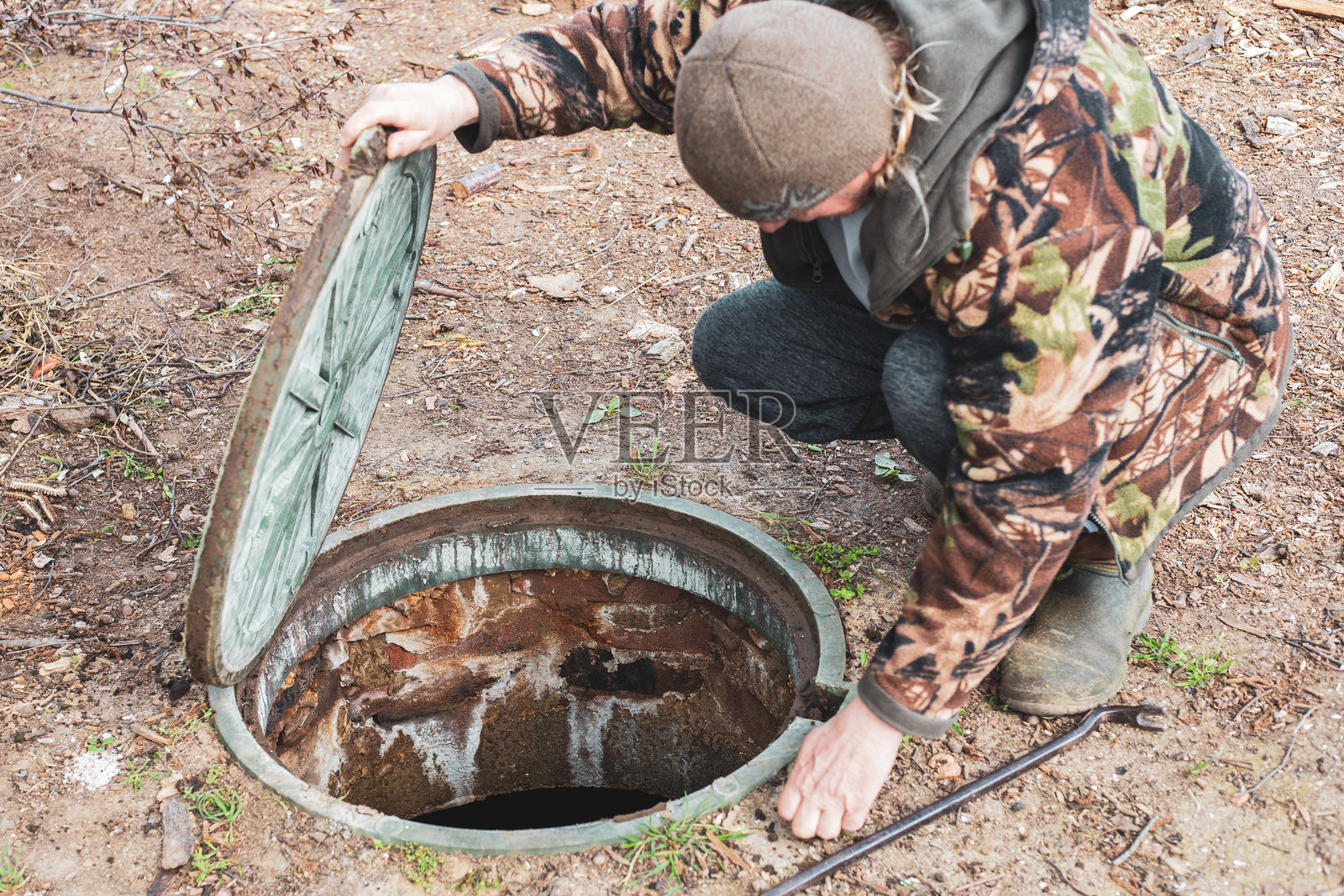 一名男子打开化粪池的舱口检查污水排放水平。乡村房屋的化粪池照片摄影图片