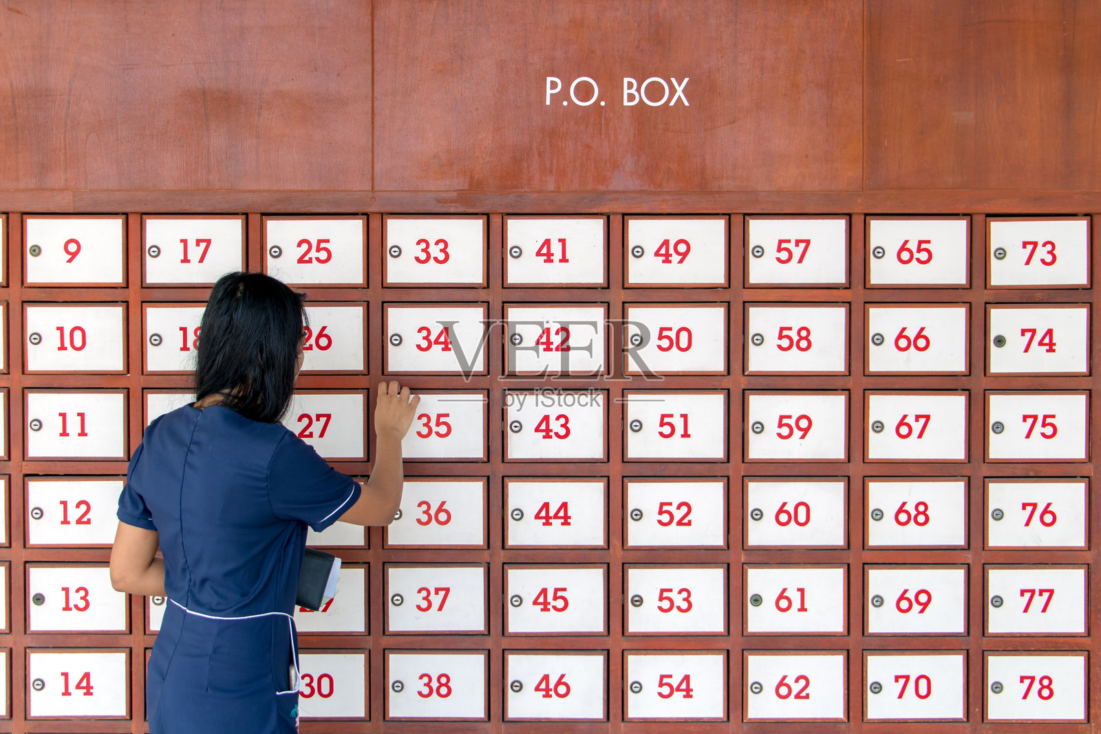 一位年轻女性在满是邮箱的墙上打开邮箱。女性正在使用墙上的投递箱。照片摄影图片