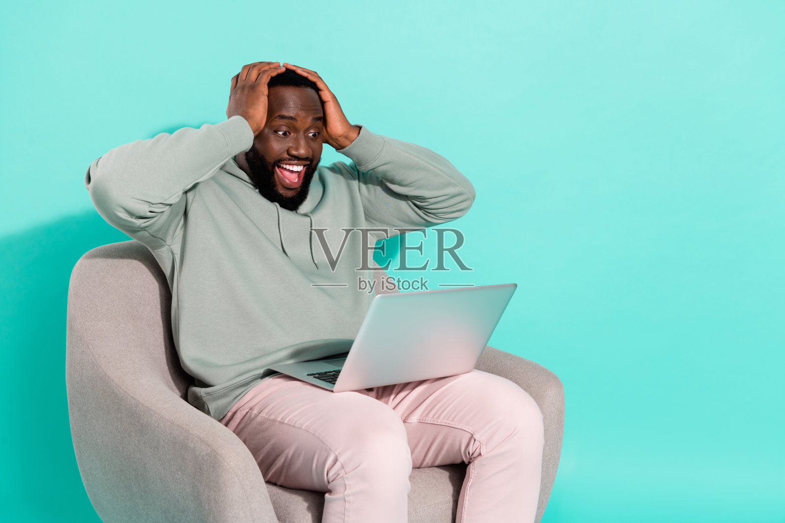 一位英俊时尚、惊讶且幸运的男士在明亮的青绿色背景下使用笔记本电脑，展现出成功项目的喜悦。照片摄影图片