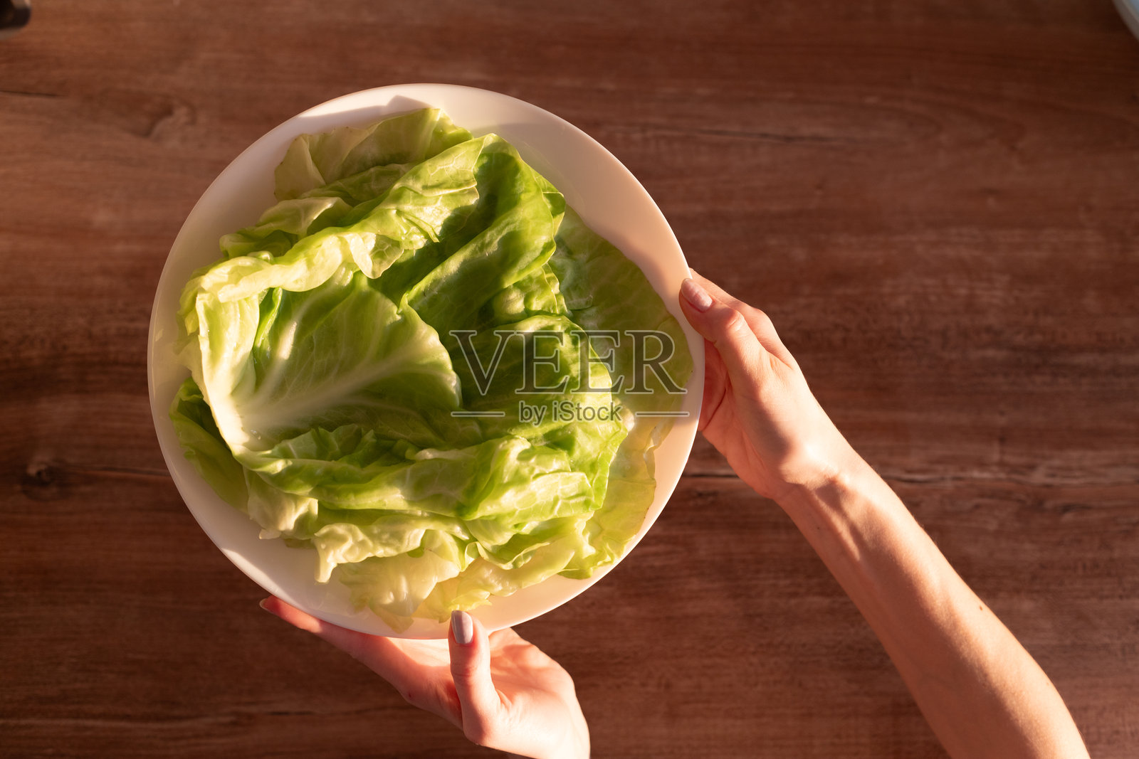 新鲜多汁的绿色生菜叶放在白色盘子上，背景为木质纹理，适合健康食谱和营养菜肴。照片摄影图片