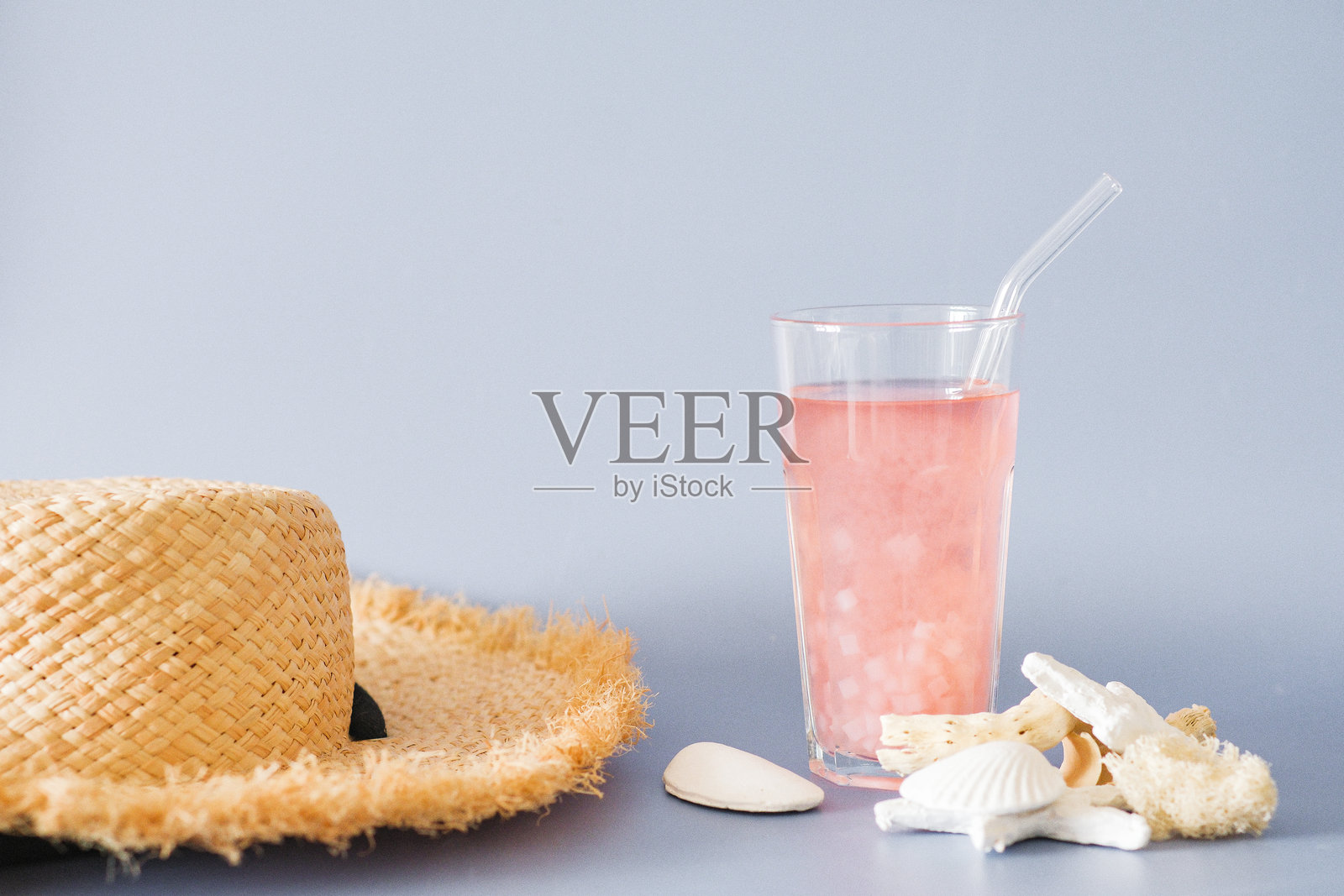 享受清爽的夏季饮品，戴着草帽，周围是贝壳。照片摄影图片