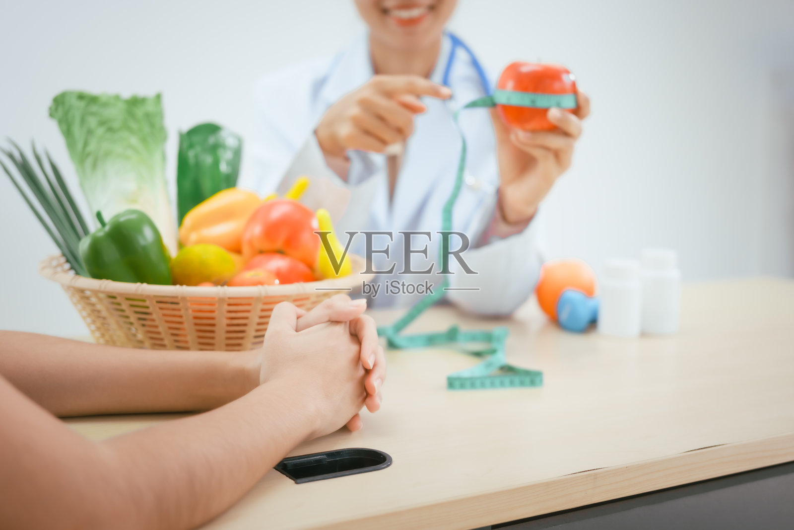 一位年轻女性营养专家在医院的办公桌前工作，咨询女性患者关于吃蔬菜和水果，推广健康饮食，提供有效减重和健康的指导。照片摄影图片