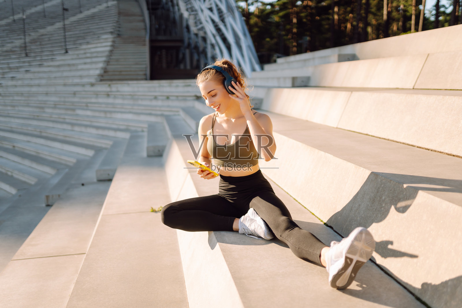 一位穿着运动服的女性在垫子上锻炼，同时在日落时分听音乐。照片摄影图片