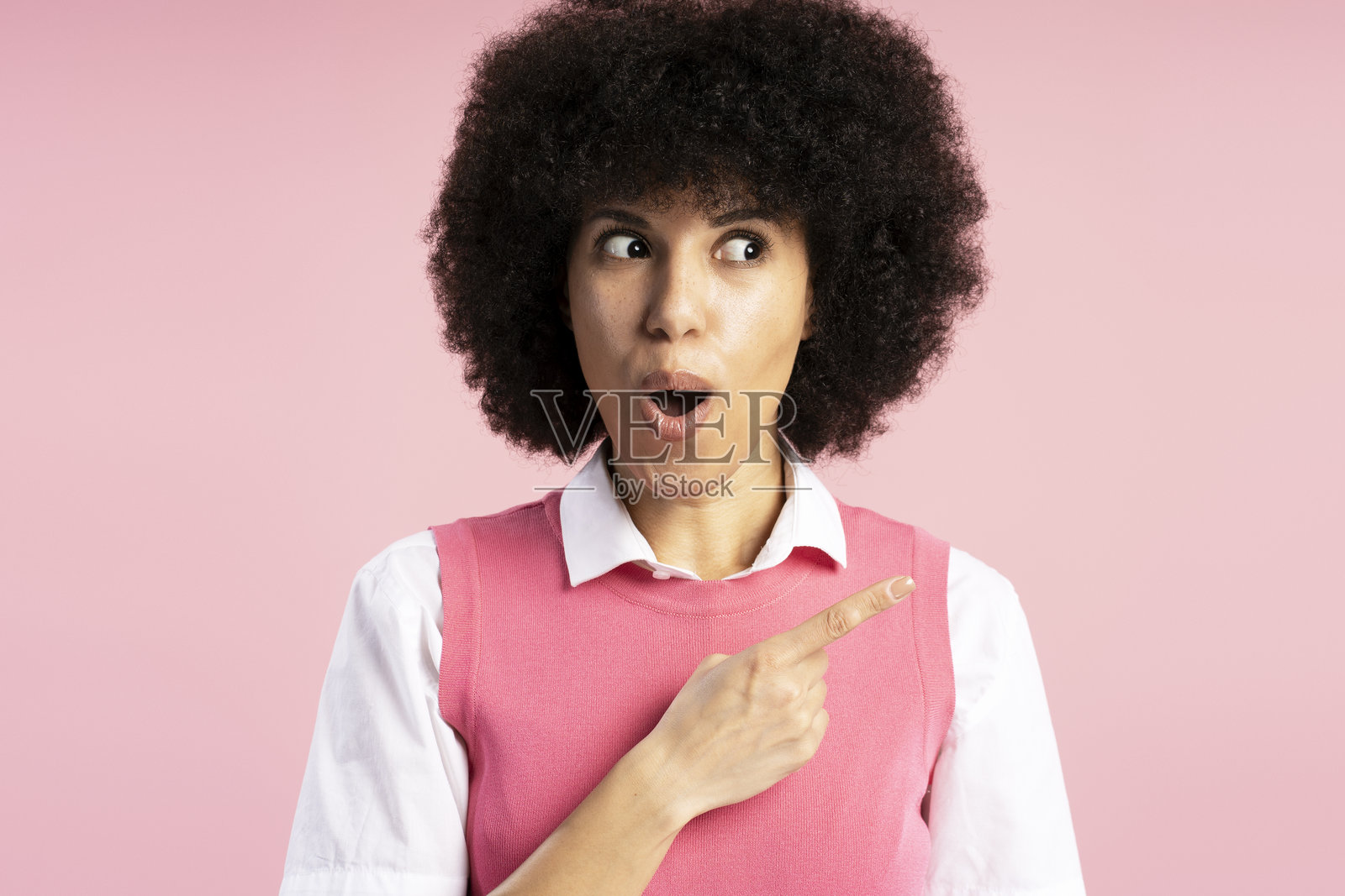 震惊的年轻女性在粉色背景上指着旁边照片摄影图片