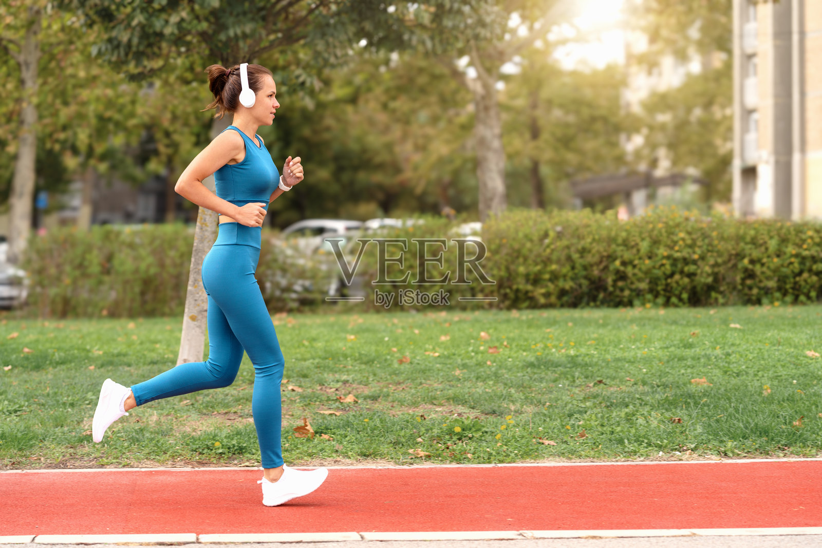 年轻女性运动员穿着运动服和耳机在城市跑道上奔跑照片摄影图片