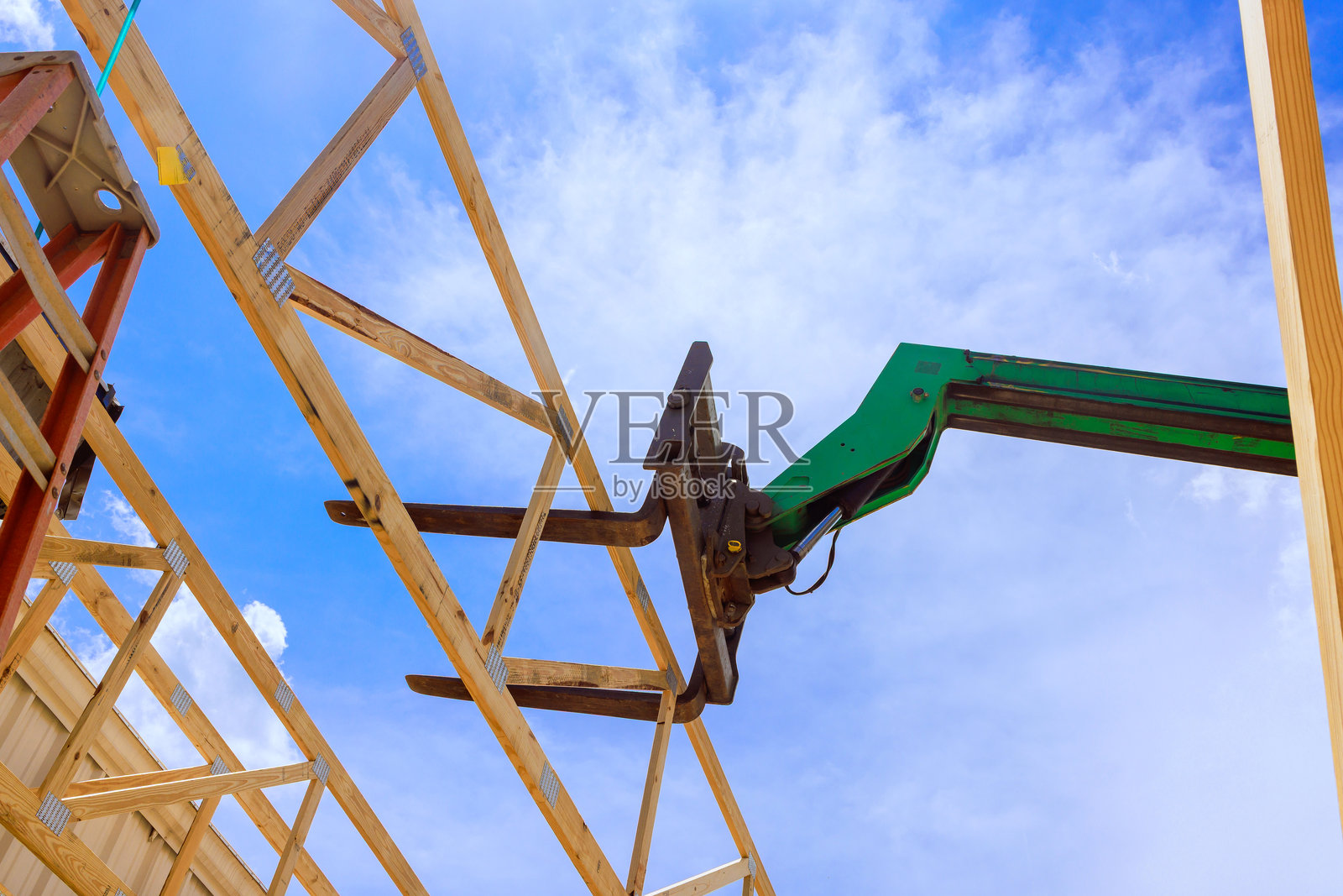 建筑工地上，机械在蓝天背景下吊起木质桁架梁照片摄影图片