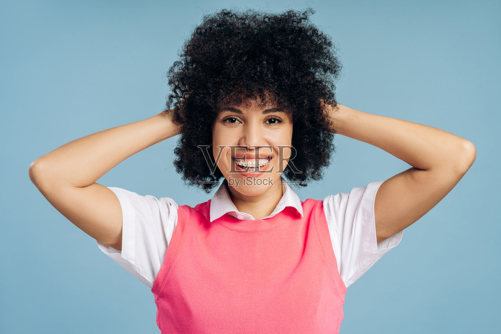 微笑的非裔美国女性，戴着牙套，微笑着并抚摸着头发，背景为蓝色。照片摄影图片