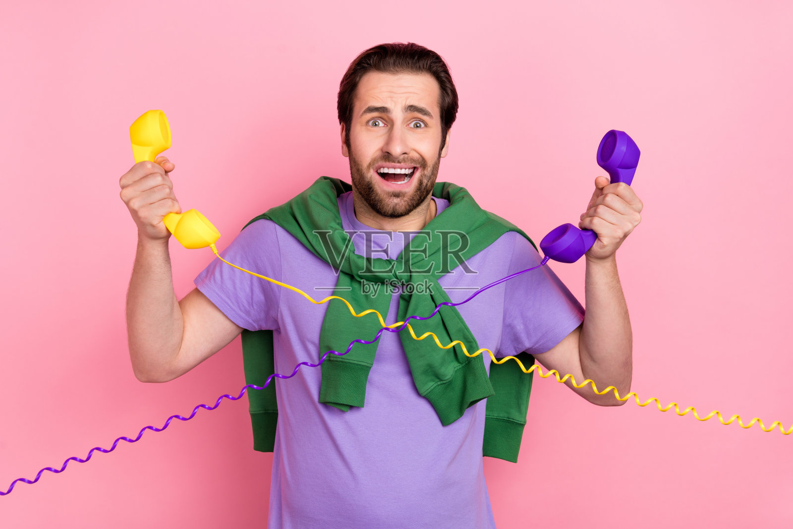 穿着T恤和毛衣的压力山大的千禧一代胡子男士在粉色背景下打电话照片摄影图片