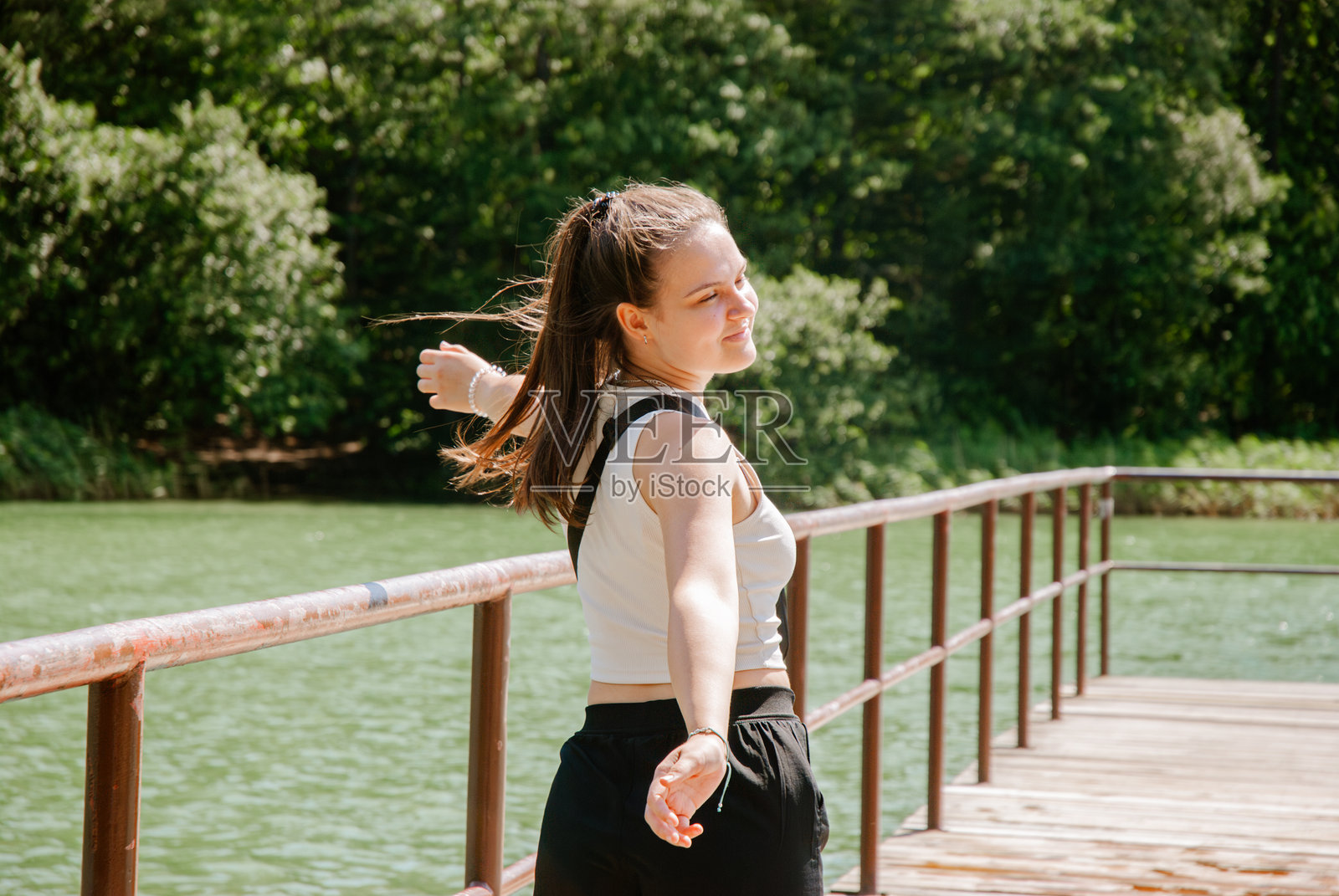 快乐的年轻女性在阳光明媚的日子里悠闲地坐在湖边的码头上。周末概念，靠近森林和湖泊。照片摄影图片