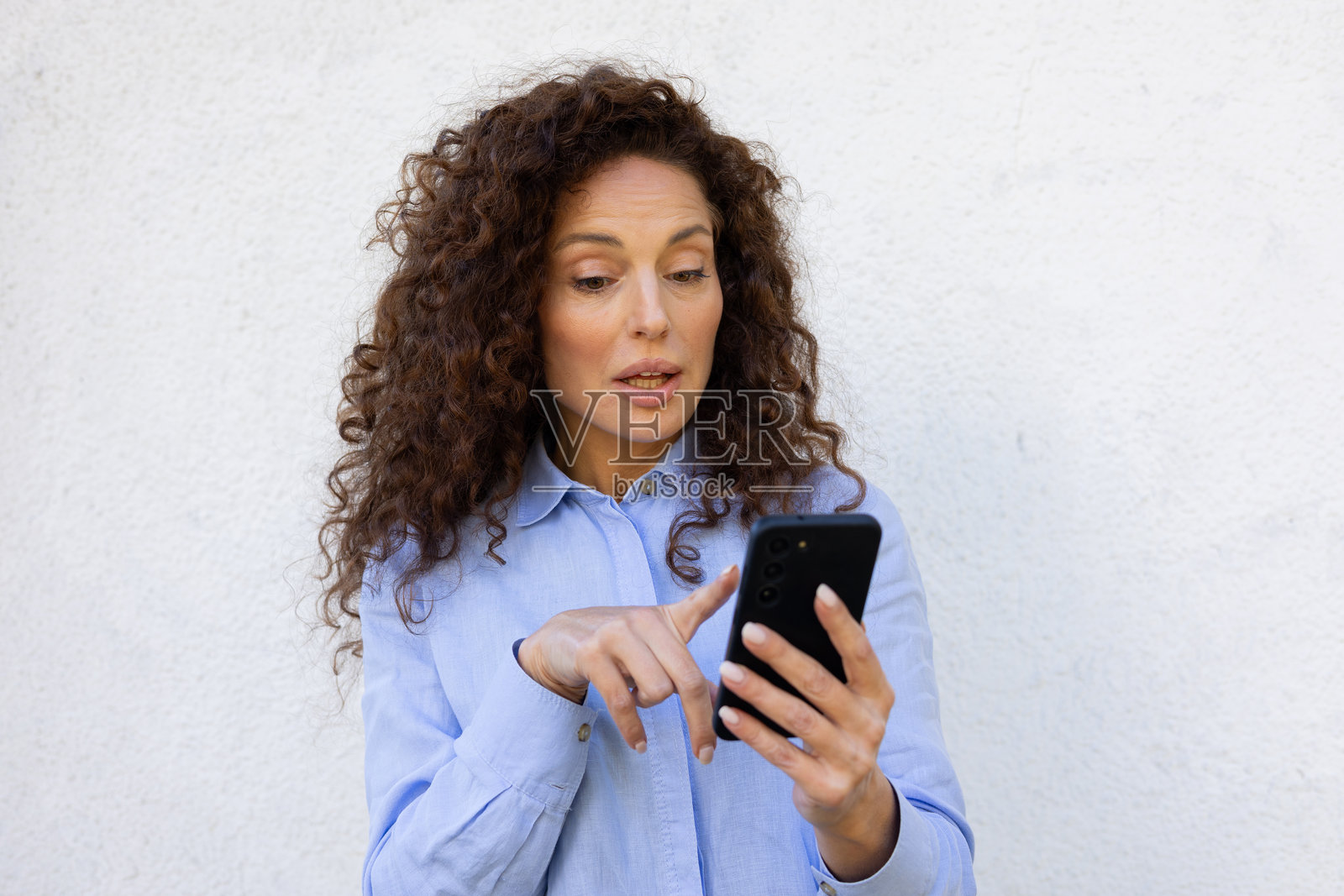 中年女商人卷发，正在手机上阅读令人震惊的新闻照片摄影图片