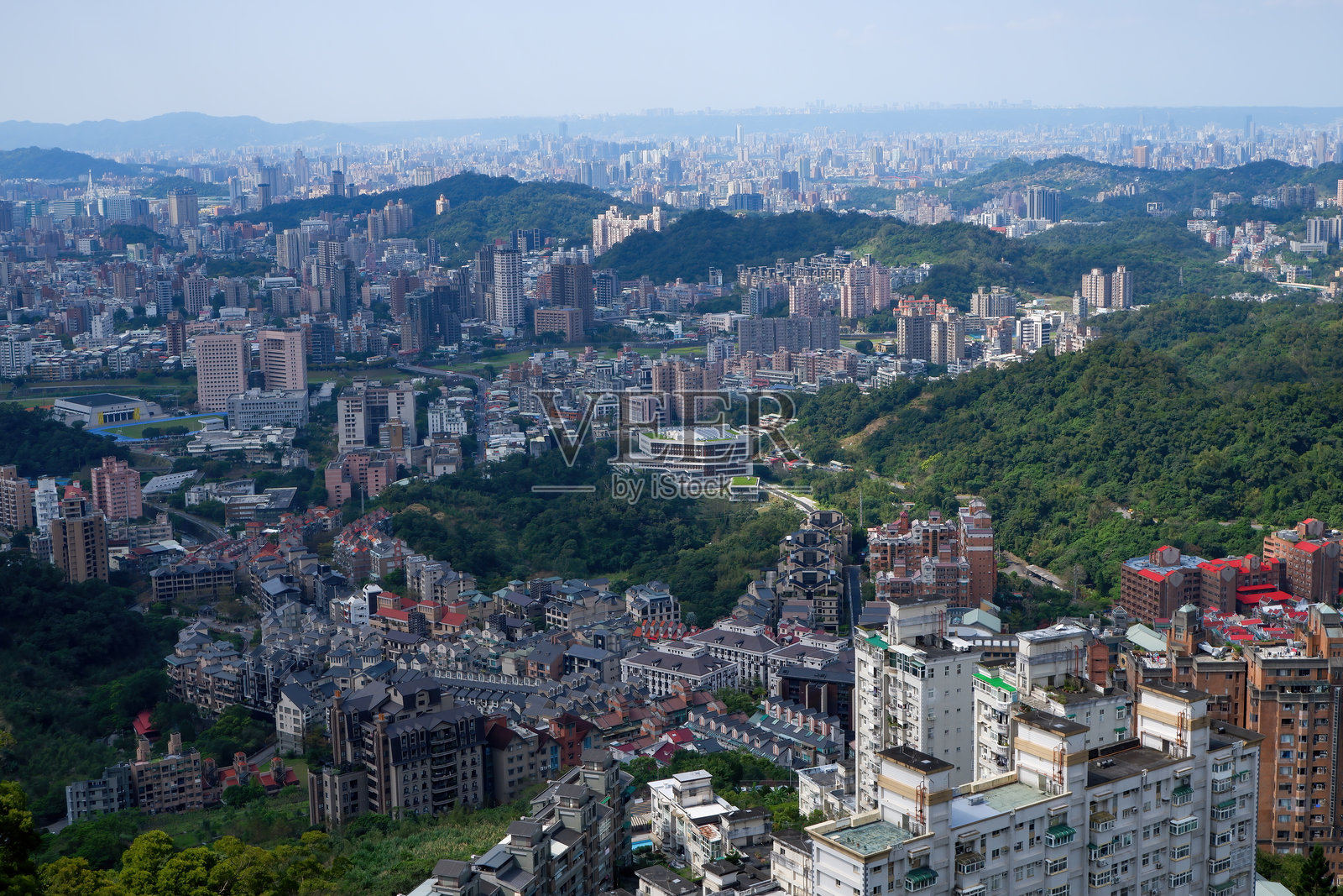郁郁葱葱的山丘间，一座 sprawling 的城市在晴朗的天空下展现出全景。照片摄影图片