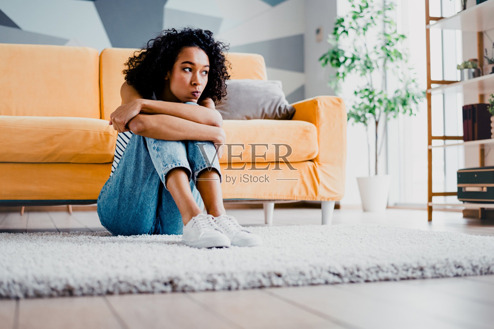 年轻女性坐在温馨明亮的客厅地毯上，沉思地反思，展现出一种轻松随意的居家生活方式。照片摄影图片