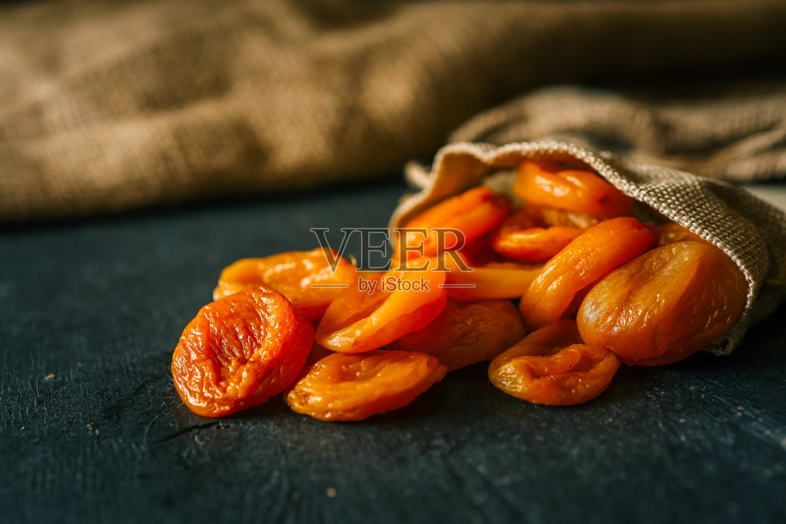 干杏干从一个质朴的麻袋中洒落在深色纹理表面上，营造出自然和有机的感觉照片摄影图片