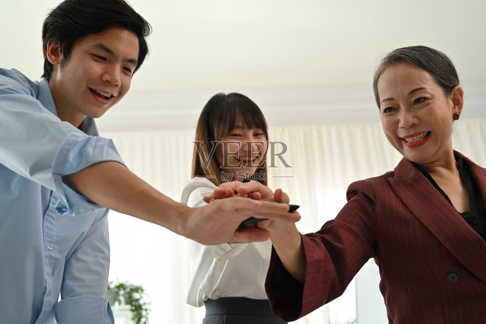 一个多元化的跨代商业团队齐心协力，展示团队合作与协作。资深领导与年轻专业人士共同庆祝成功、尊重、指导和共同目标。照片摄影图片