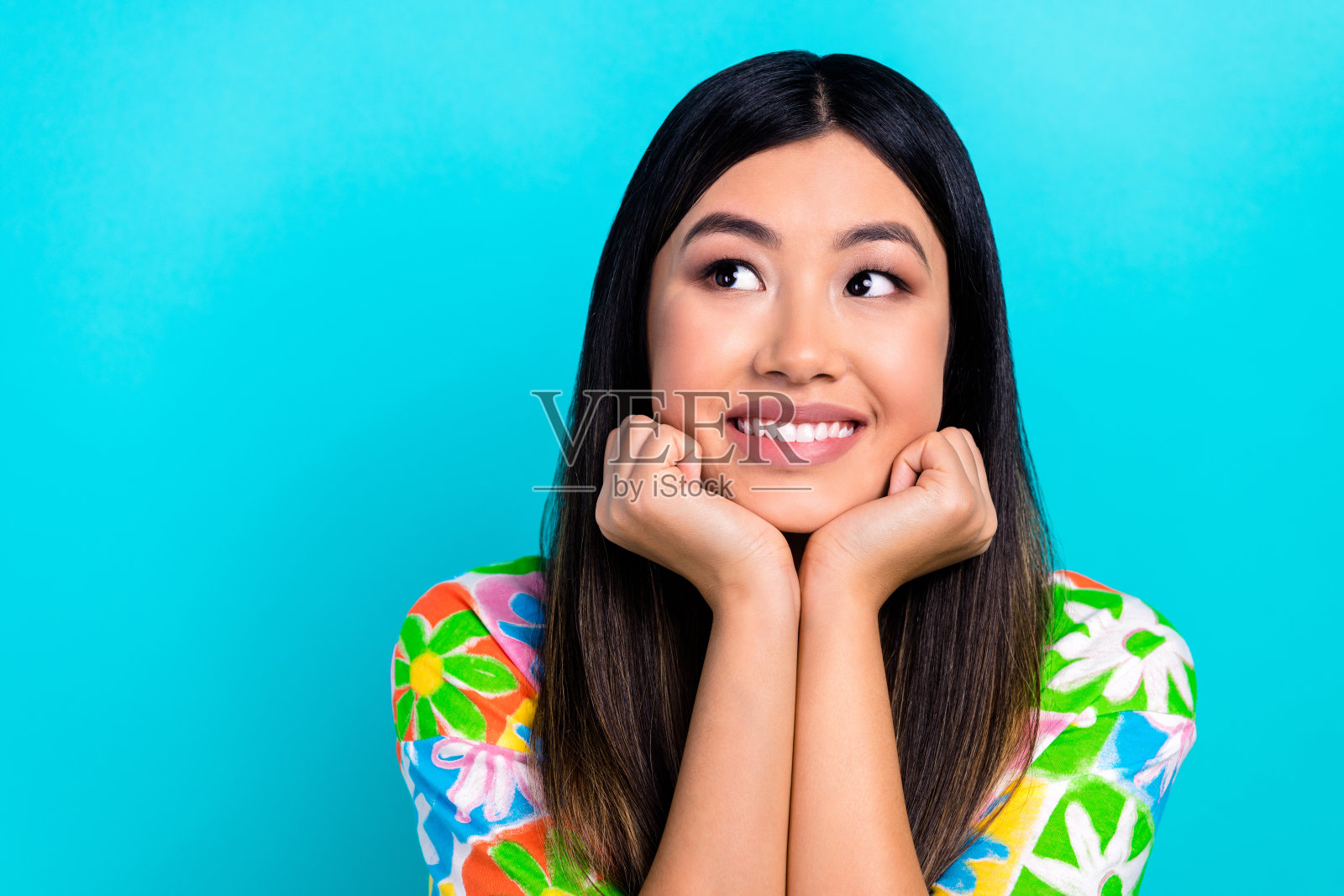 穿着花卉印花T恤的积极思考女性，双臂托腮，凝视空旷的空间，背景为青绿色。照片摄影图片