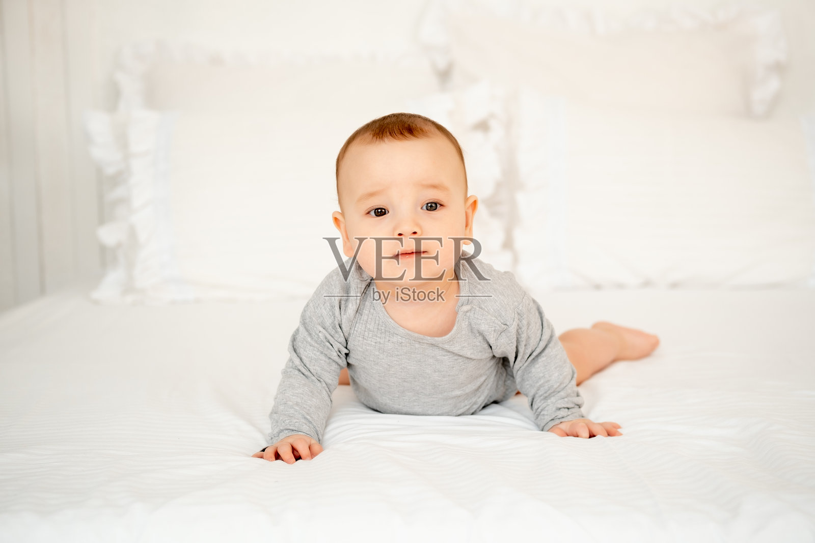 一个六个月大的可爱男婴躺在卧室的白色床上，留有文字空间照片摄影图片