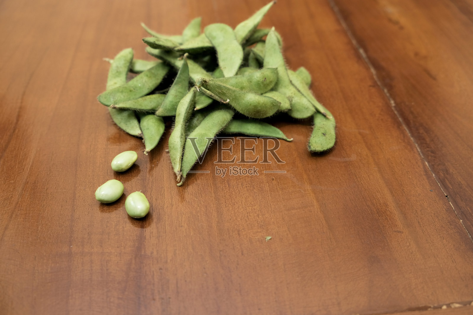 新鲜的绿毛豆荚。木桌上堆放着新鲜的黄豆荚。照片摄影图片