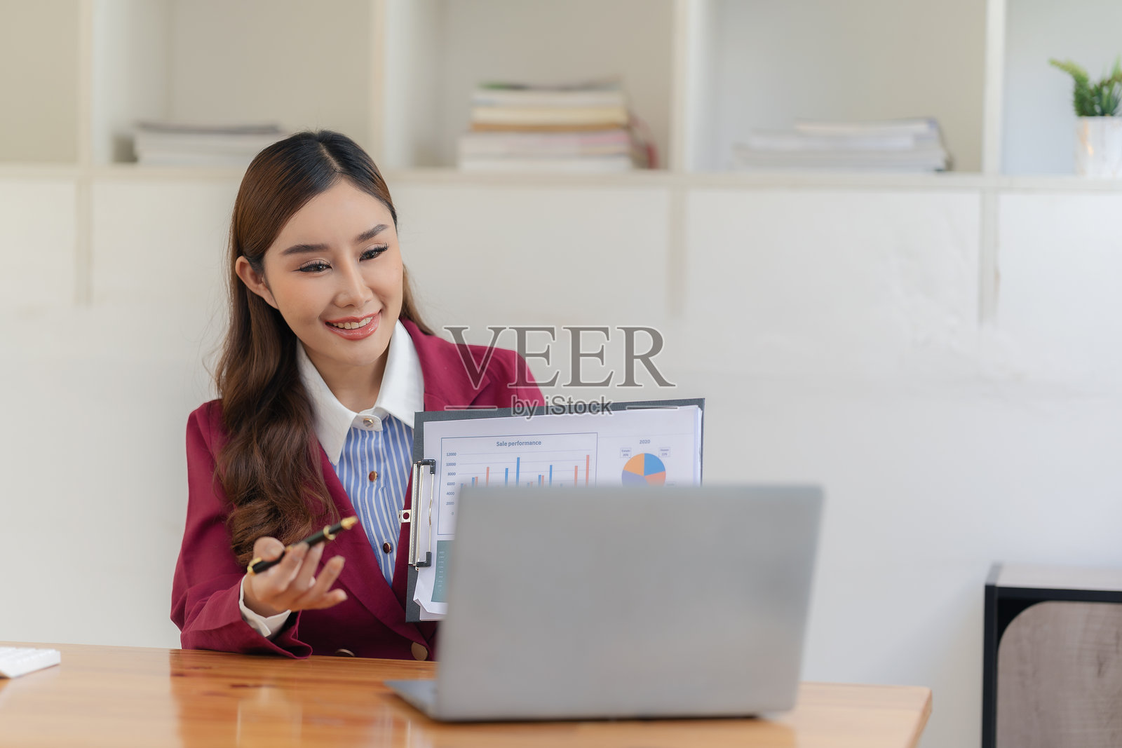 微笑的亚洲会计师正在使用计算器分析财务文件，并在桌子上使用笔记本电脑工作。照片摄影图片