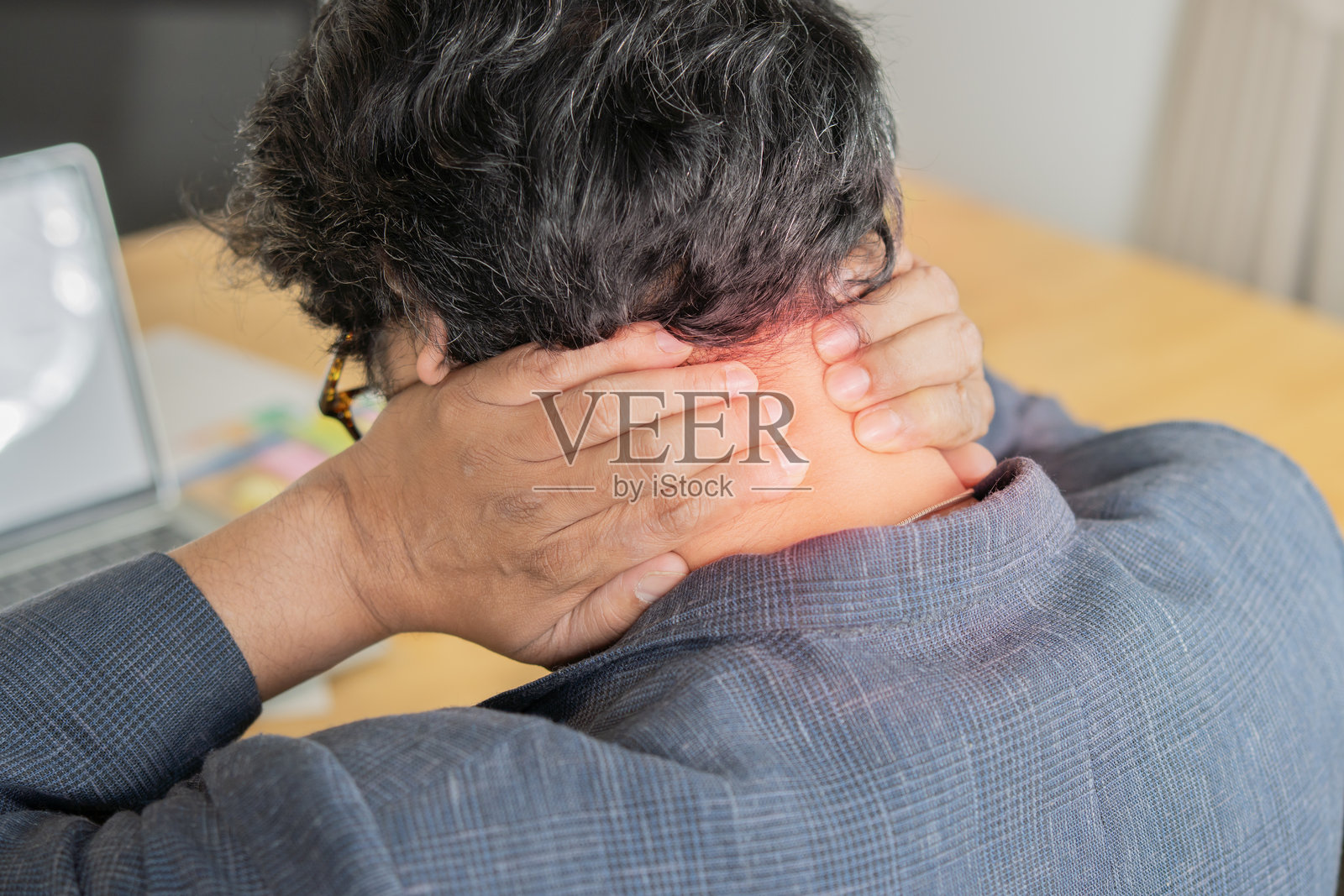 成熟的亚洲商务男士背影，穿着西装，在办公室的桌子上使用电脑，感到颈部疼痛。照片摄影图片