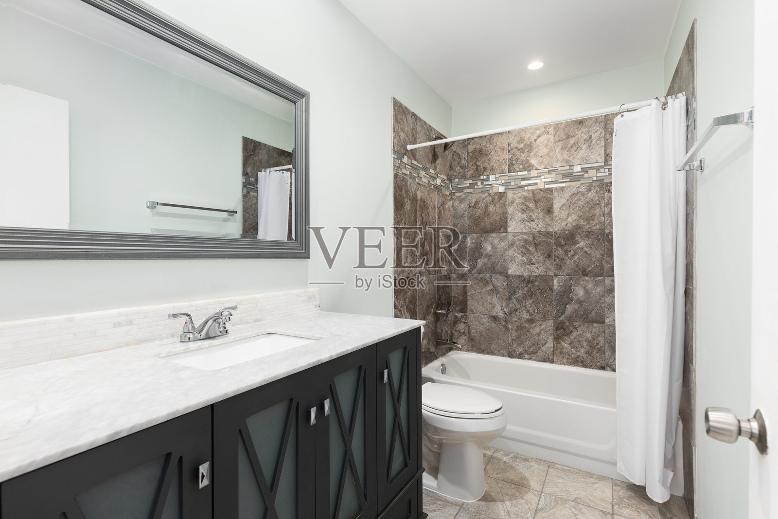 一个带有灰色橱柜和棕色瓷砖淋浴的浴室。照片摄影图片