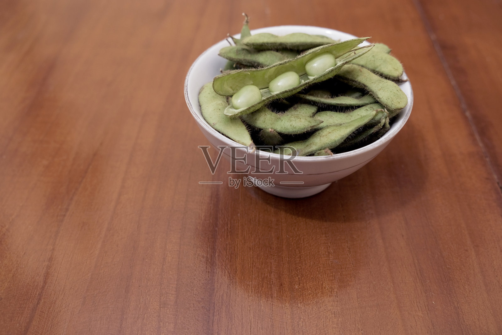 生的绿色毛豆荚。新鲜的黄豆荚堆放在木桌上的白色碗里。照片摄影图片