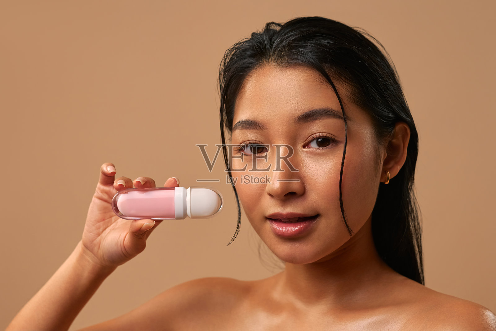 在米色背景下涂抹唇彩的亚洲女性照片摄影图片