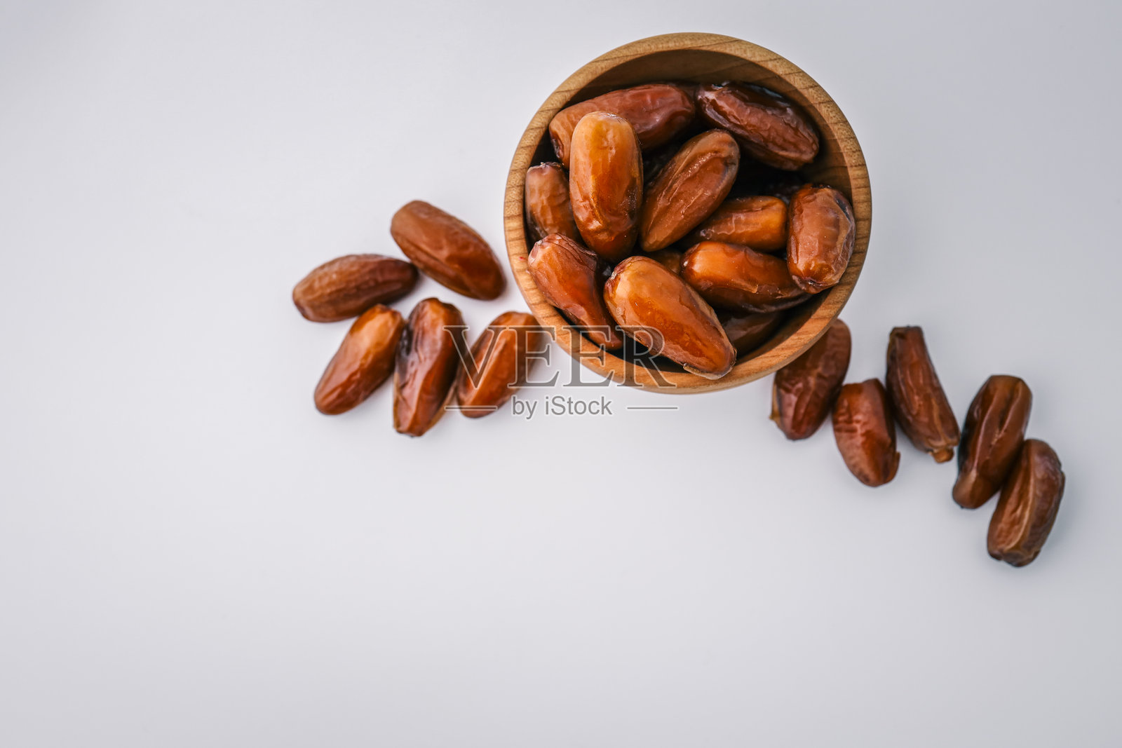 圆木碗中装满了整颗枣子，周围散落着一些，背景为干净的白色。极简主义，健康食品概念，展现自然干果。照片摄影图片