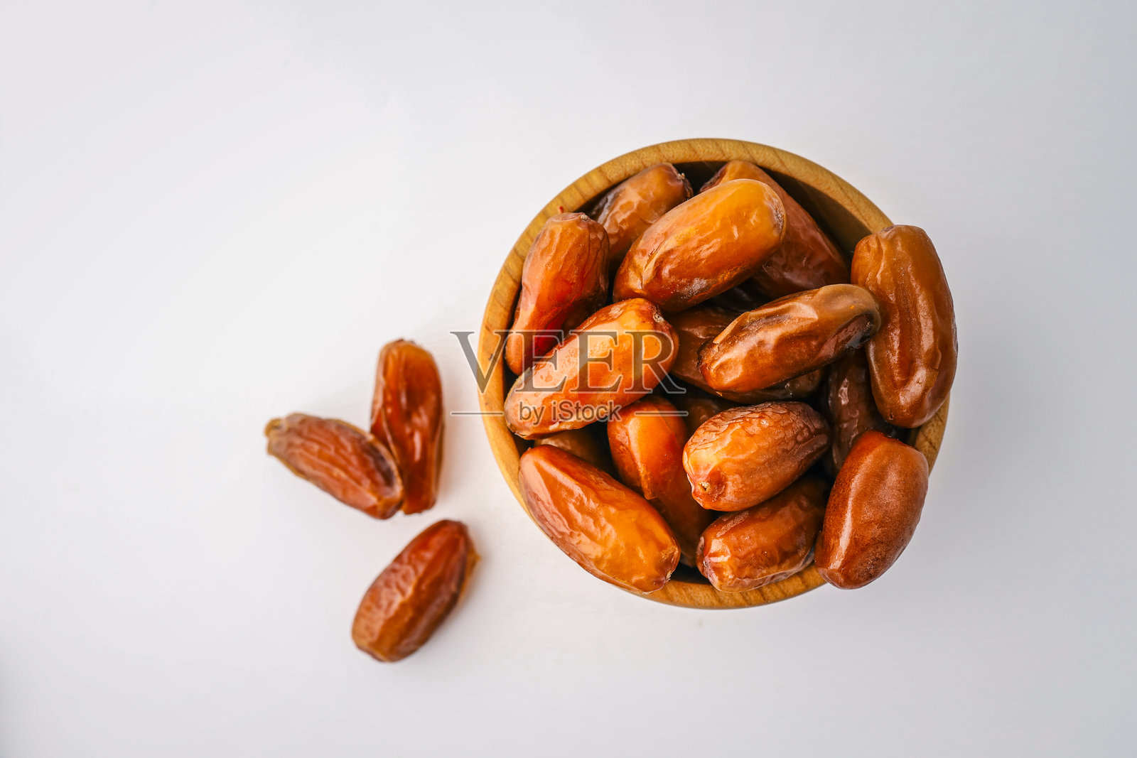 圆木碗中装满了整颗枣子，周围散落着一些，背景为干净的白色。极简主义，健康食品概念，展现自然干果。照片摄影图片