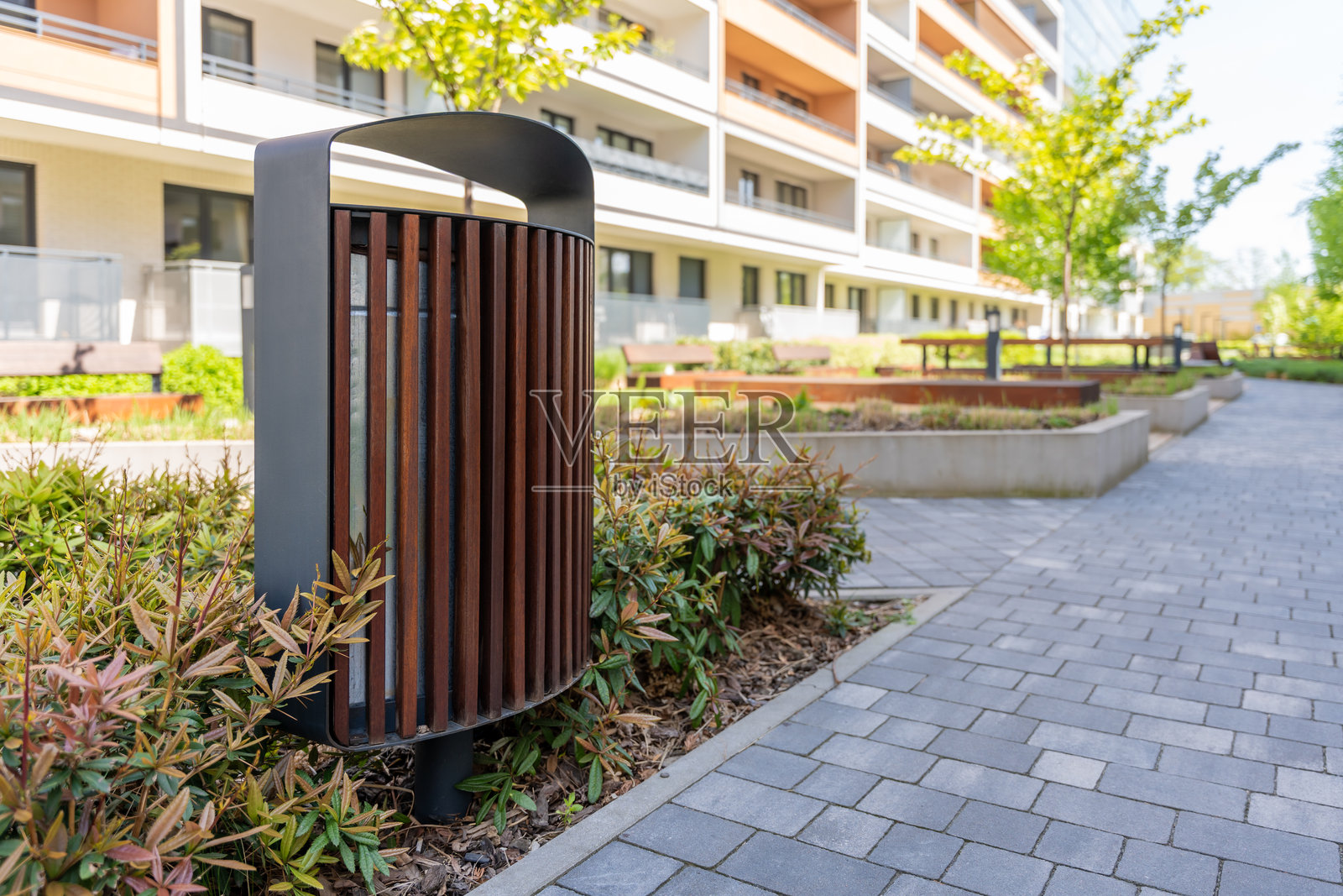 现代公寓建筑的景观庭院中，带有黑色框架的木条垃圾桶，展示了城市家具设计。照片摄影图片