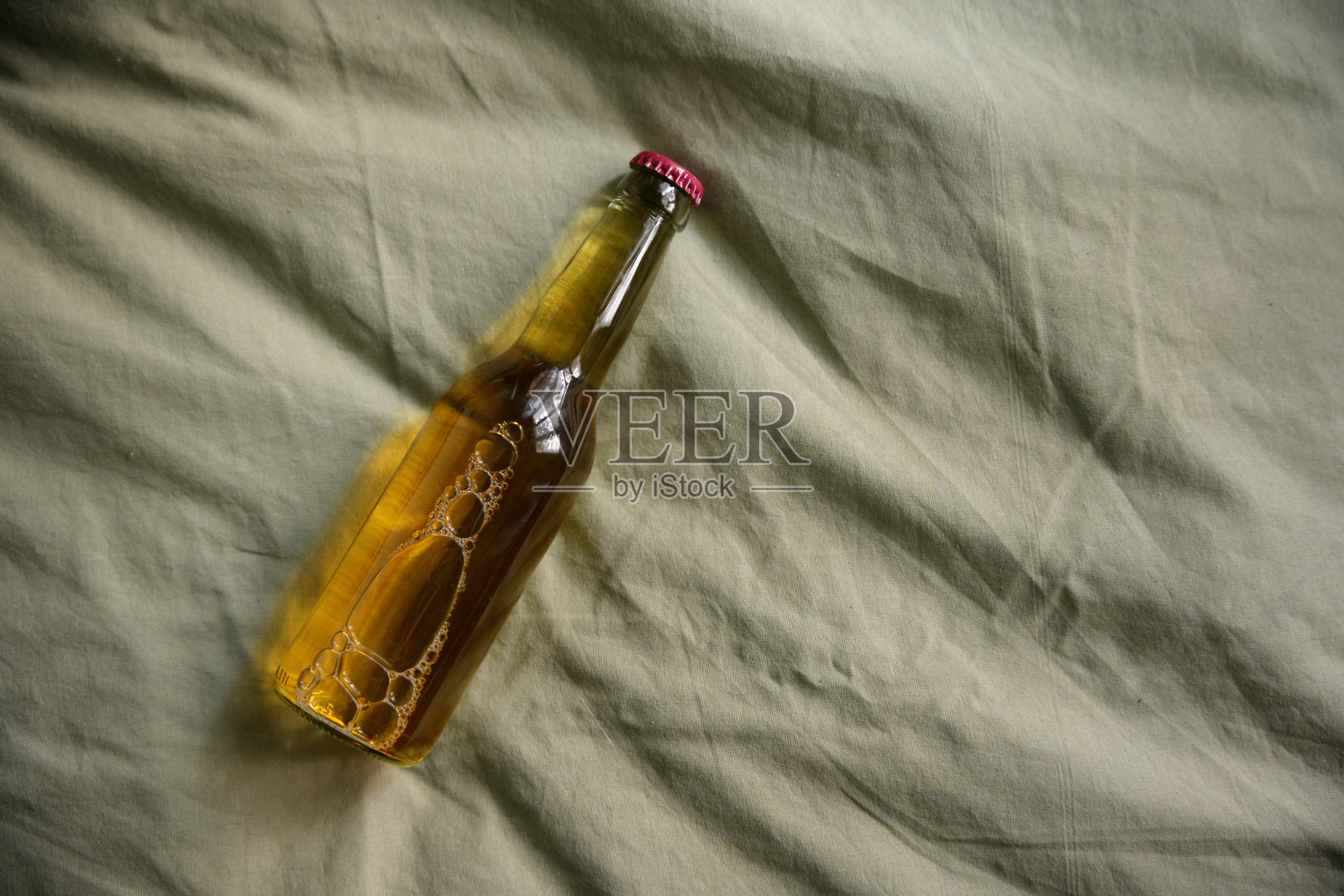 玻璃啤酒瓶躺在绿色亚麻床单上，气泡上升到表面照片摄影图片
