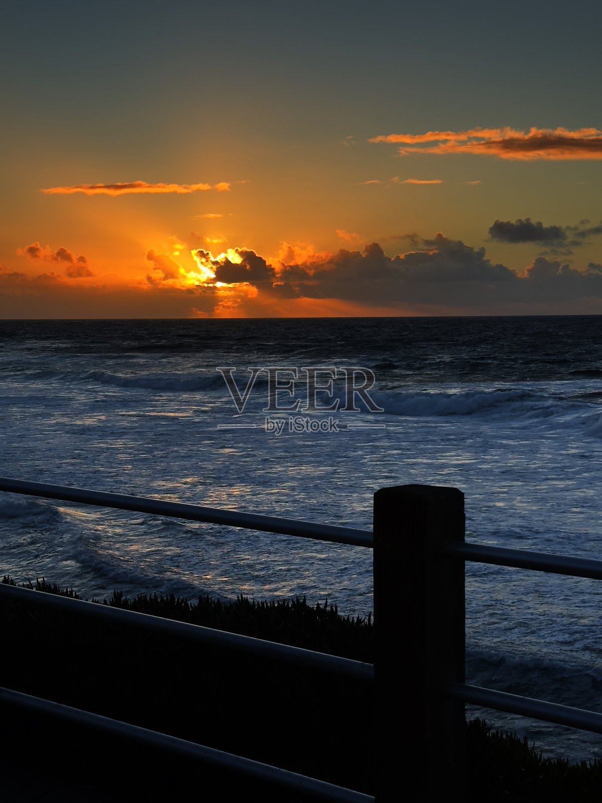 拉荷亚海湾日落的肖像照片，前景有栅栏照片摄影图片