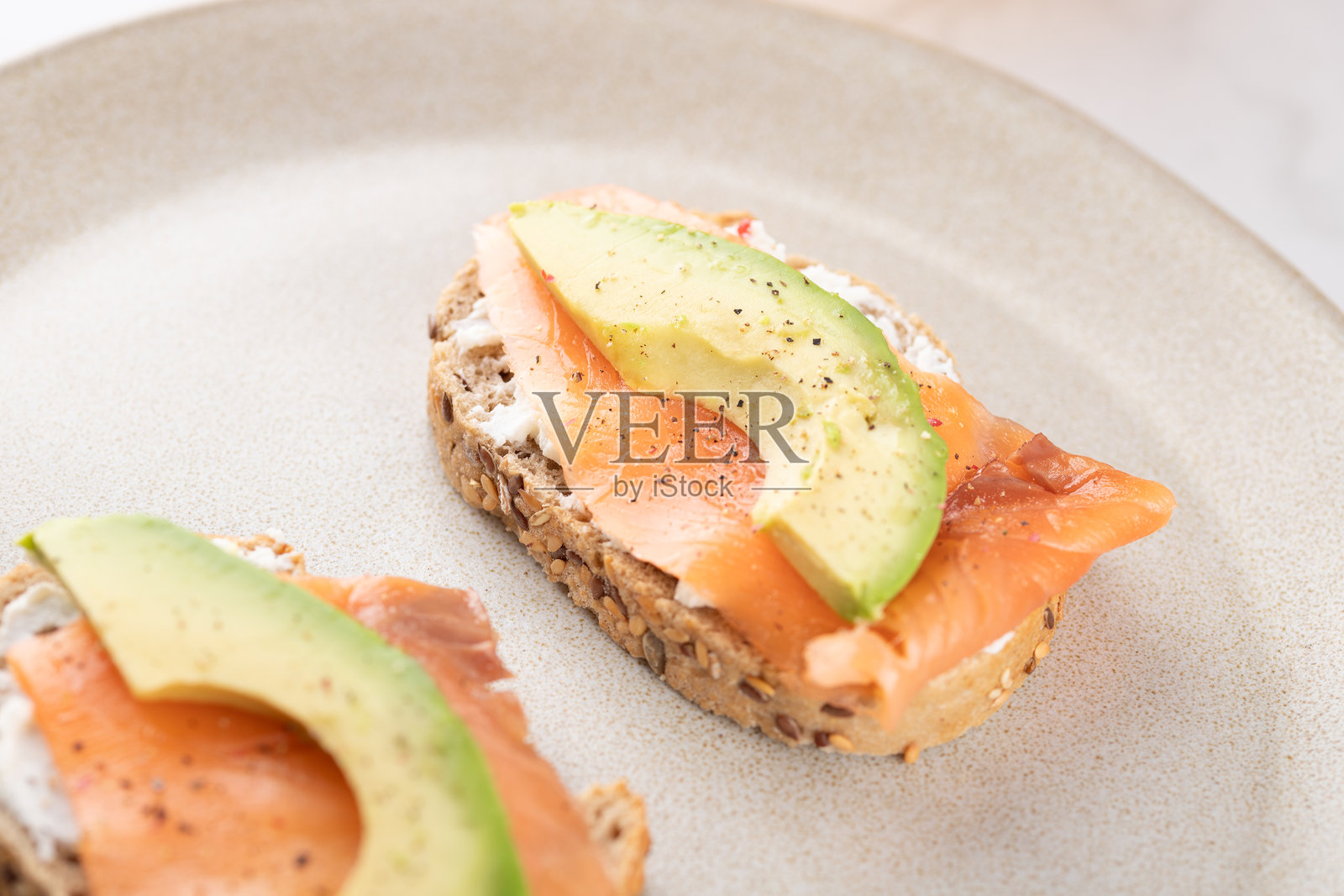 健康的全麦面包上放着鳄梨、三文鱼和奶油奶酪的特写。均衡自然的饮食。健康早餐的概念。照片摄影图片