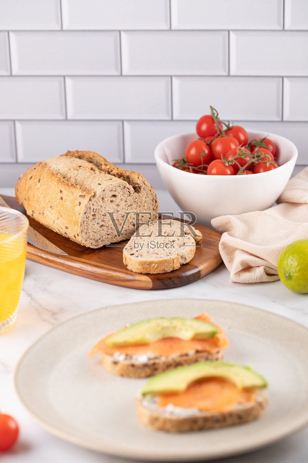 全谷物种子面包放在木板上，旁边是装有樱桃番茄的白色碗，背景中有健康的早餐。明亮的场景中充满自然食材。照片摄影图片