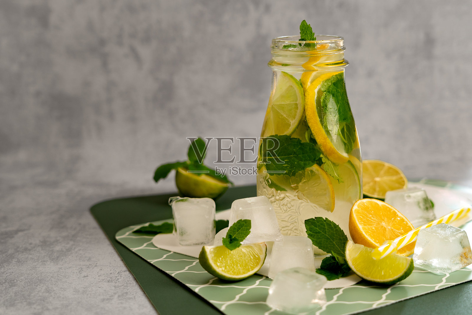 玻璃罐中的柑橘排毒茶，配有青柠、柠檬、薄荷和冰块，背景为灰色。夏季柠檬水制作的概念。照片摄影图片