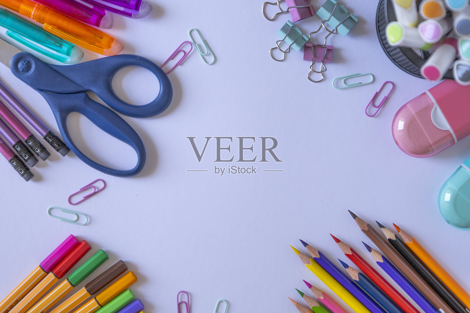 一组色彩丰富的办公和学校用品整齐地展示在白色表面上。包括铅笔、马克笔、剪刀、回形针、夹子和橡皮擦。非常适合教育用途。照片摄影图片