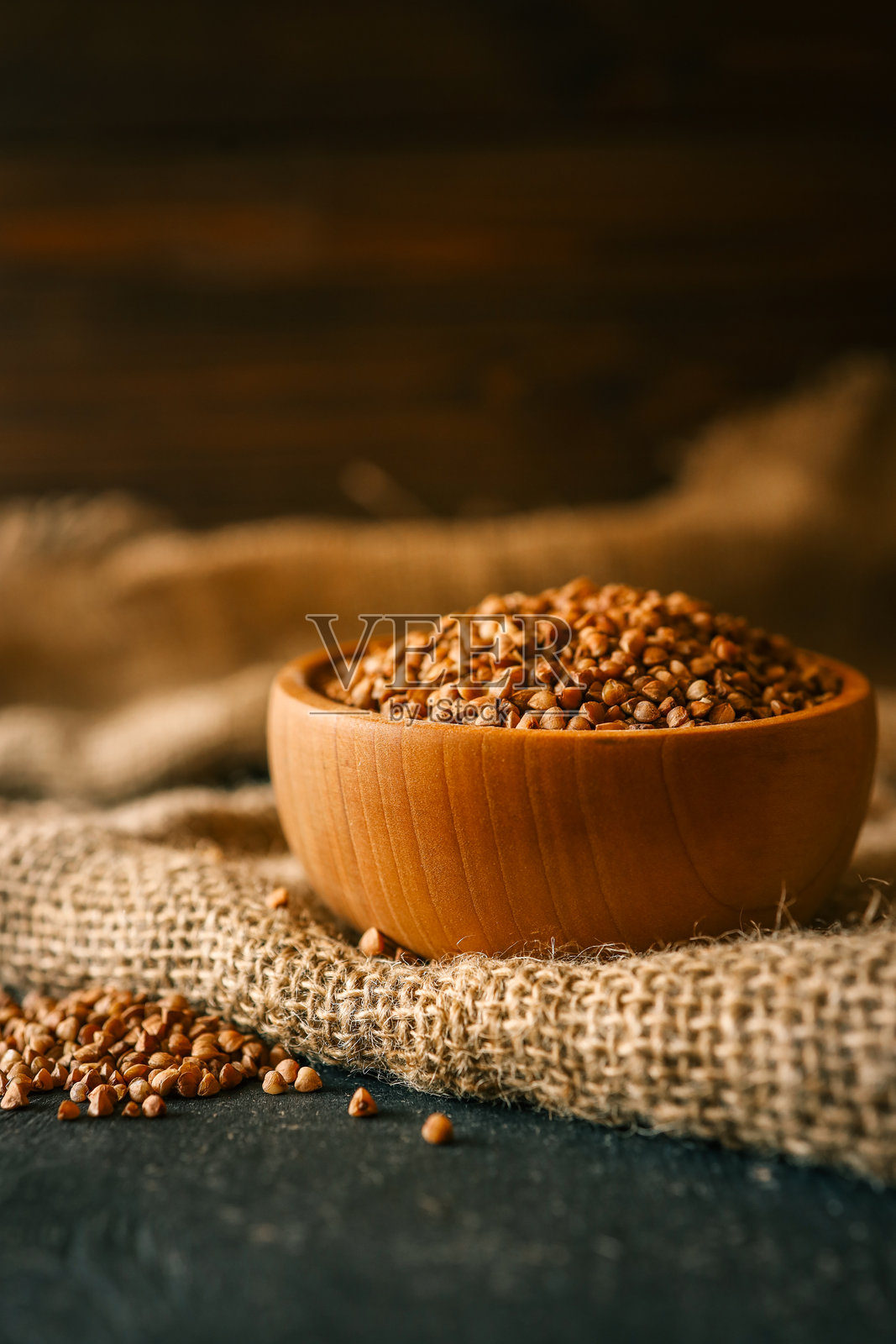 装满生荞麦粒的木碗放在质朴的麻布上。自然环境中的健康有机食品，温暖的色调和选择性焦点。照片摄影图片